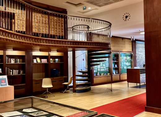 na pierwszym planie wystawa, na drugim - regał z książkami i schody kręcone