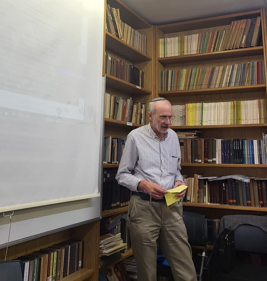 człowiek w jarmułce stojący przed tablicą, w tle regały z książkami